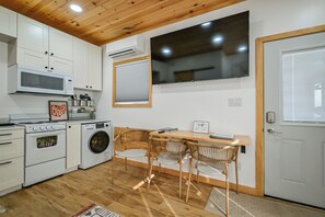 A compact kitchen with white cabinets, a microwave, a stove, and a washing machine. There is a wooden dining table with two chairs and a TV mounted on the wall. - "Tiny Tranquility" The Luxury Tiny House (Athens)