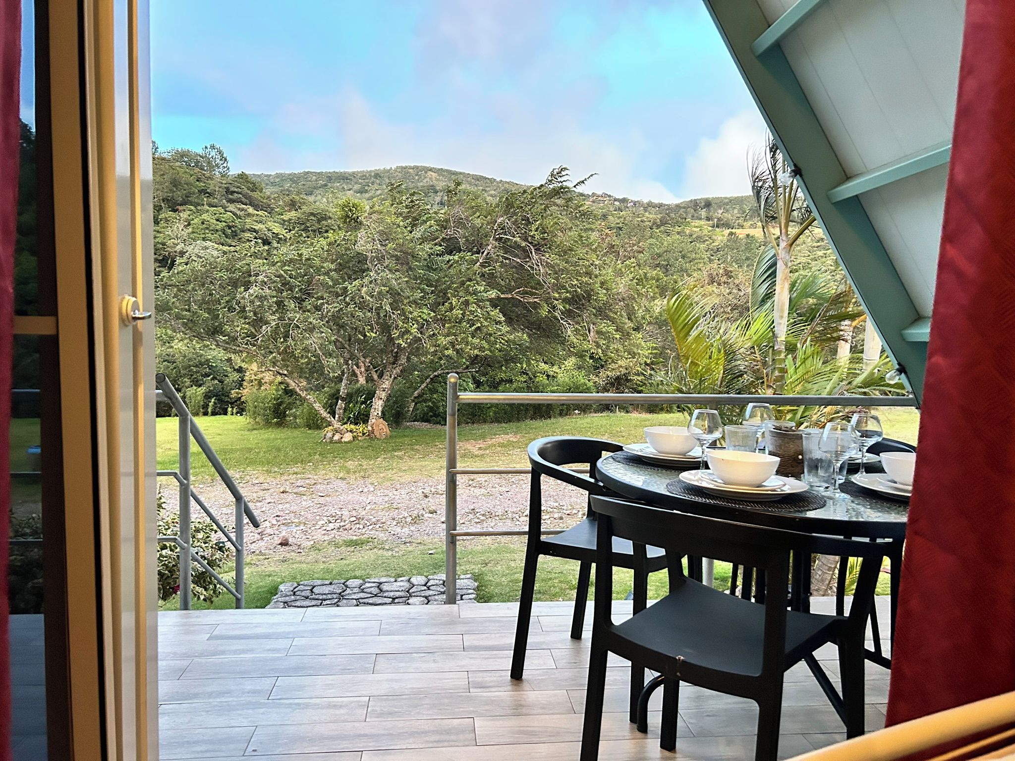 Un área de comedor con una mesa lista para dos personas, con vistas a un paisaje exuberante con árboles y colinas.