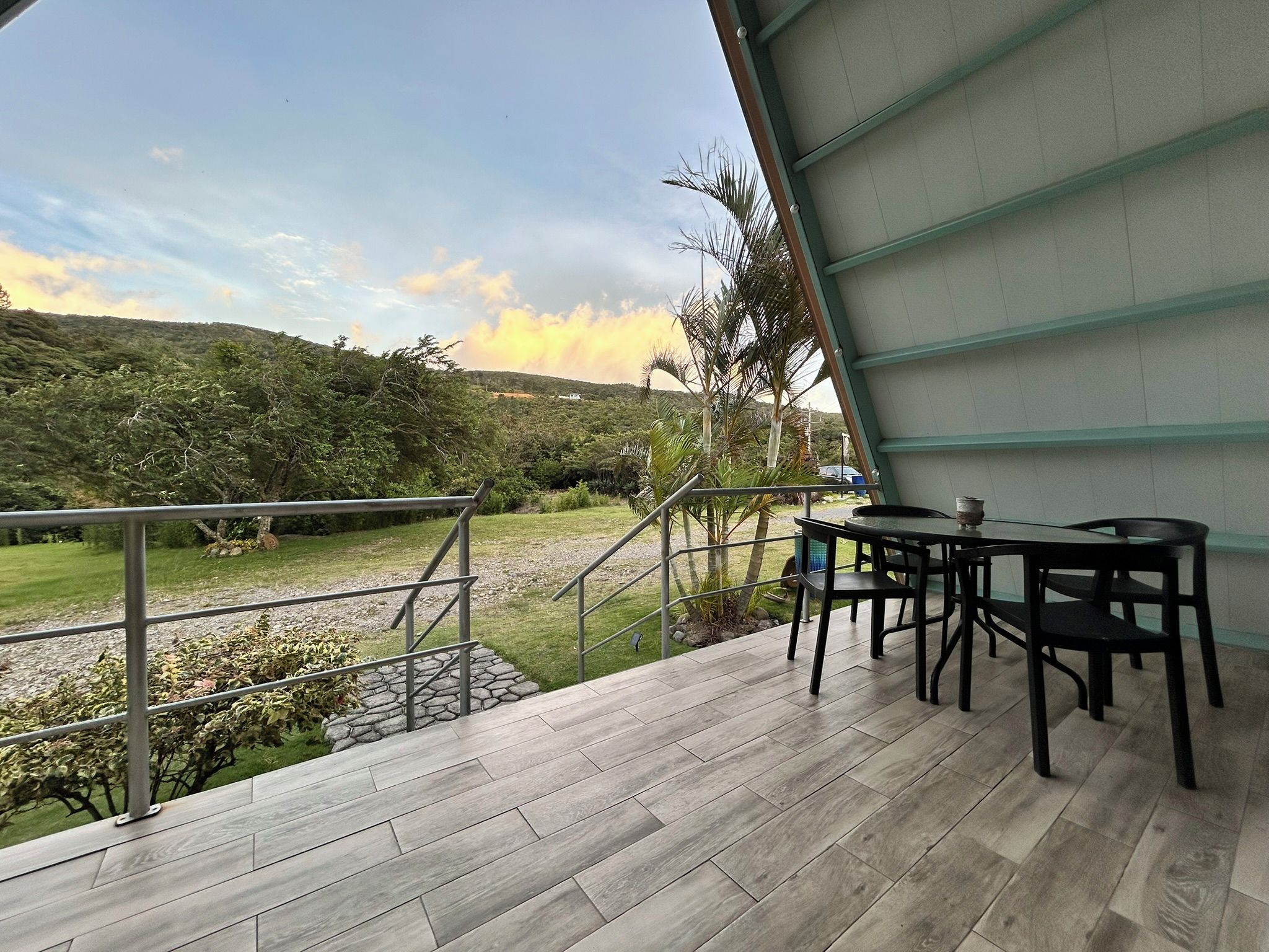 Una terraza con mesa y sillas, barandilla metálica y vista a un paisaje montañoso.