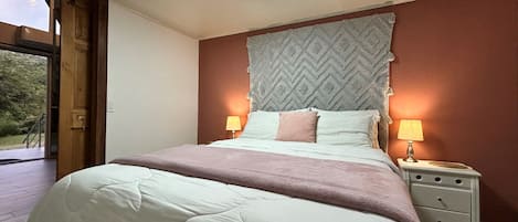 Un dormitorio con cama, lámparas de noche, mesita de noche y vistas a través de un ventanal abierto.