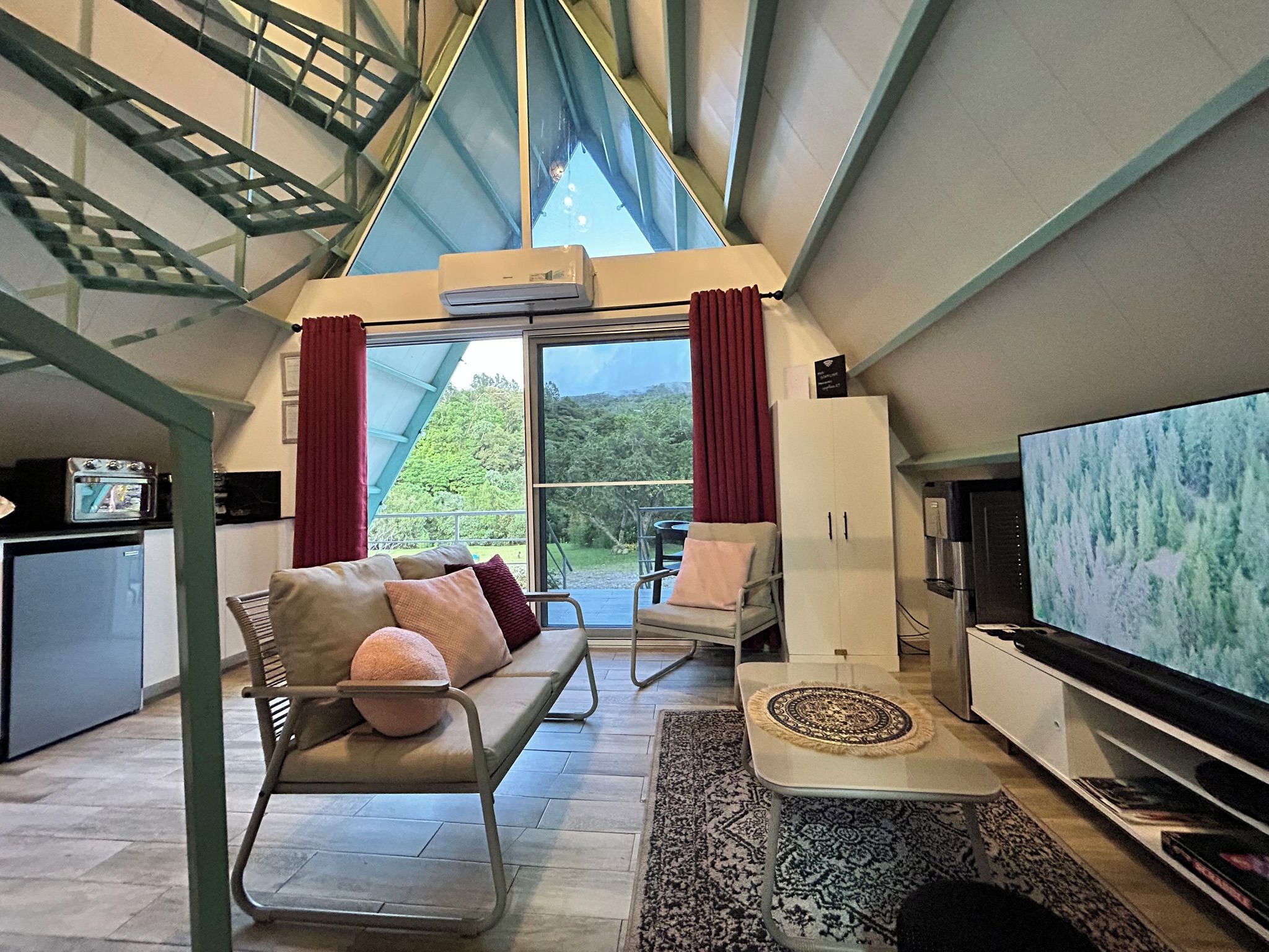 Un salon moderne avec un canapé, des fauteuils, un téléviseur et une vue sur la verdure grâce à de grandes fenêtres.