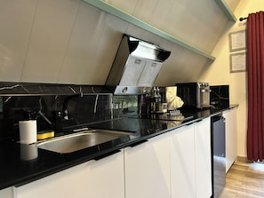 A modern kitchen with a black countertop, stainless steel appliances, and a window with curtains.