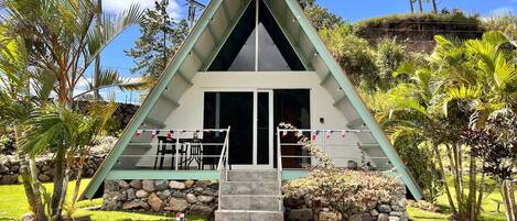 A triangular building with a stone foundation, a glass door entrance, and a small outdoor seating area with chairs.