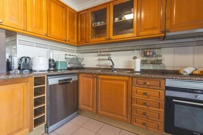 Cozinha com armários de madeira, lava-louças, fogão e diversos eletrodomésticos.