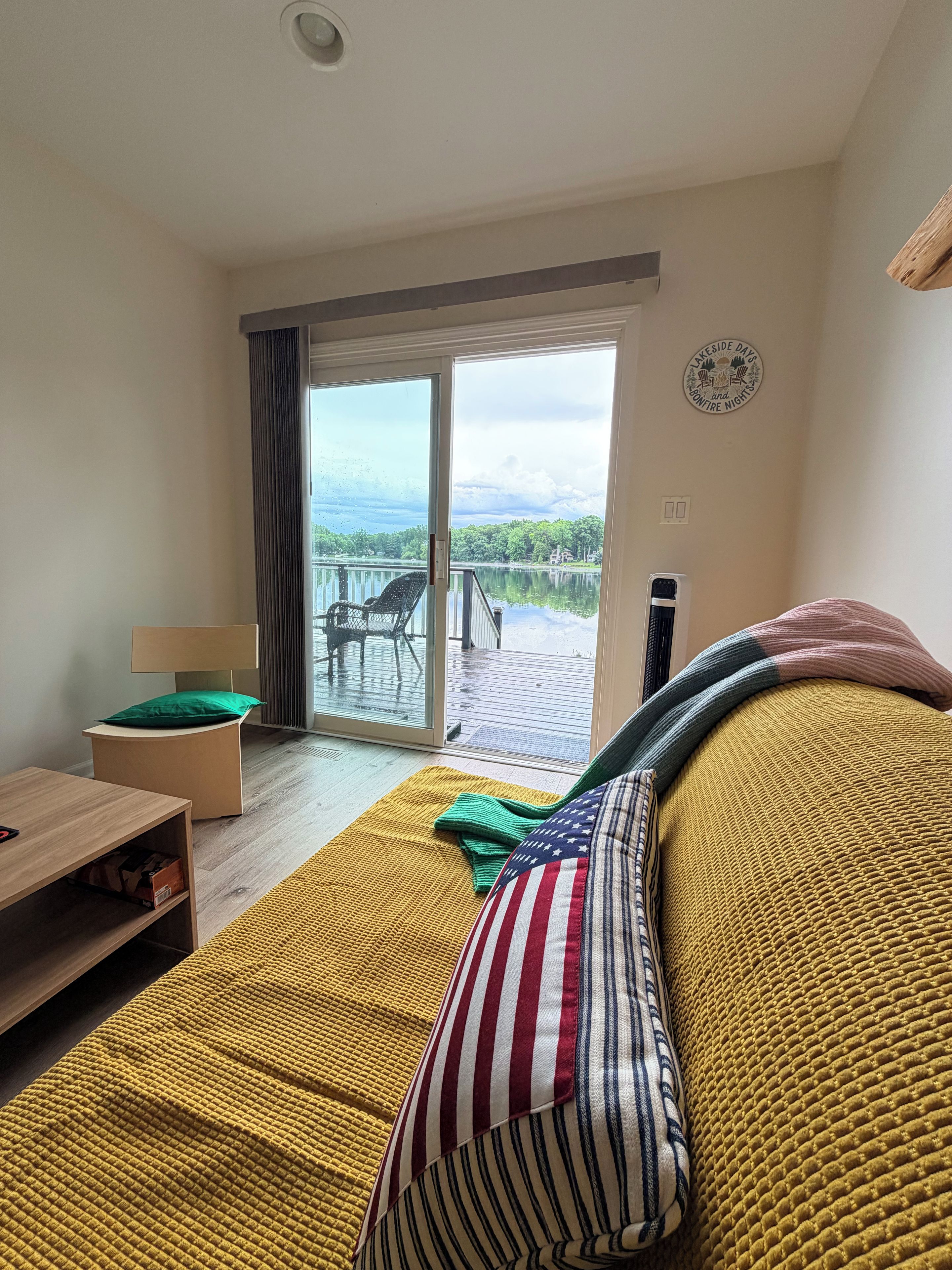 A room with a sofa, a table, a chair, and a view of a lake through a sliding glass door.