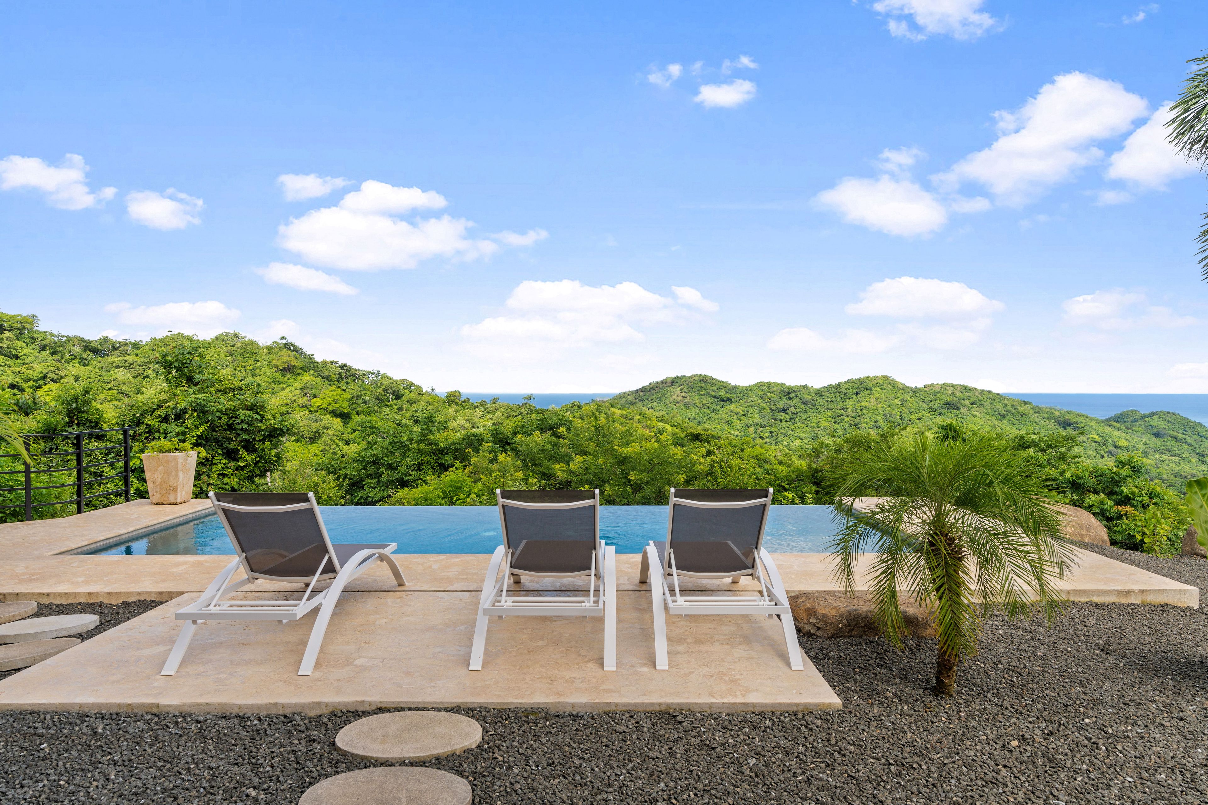 Área de piscina com três espreguiçadeiras e vista para uma paisagem montanhosa.