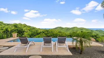 Área de piscina com três espreguiçadeiras e vista para uma paisagem montanhosa.