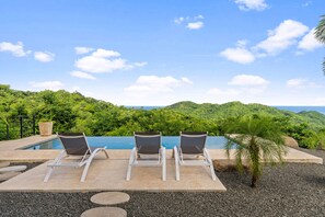 Un espace aménagé au bord de la piscine, avec trois chaises longues et une vue sur un paysage montagneux.