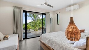 Un dormitorio con una cama, ventilador de techo, ventana grande y aire acondicionado.
