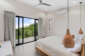 Une chambre moderne avec un grand lit, un ventilateur de plafond et une vue sur la verdure, visible à travers la porte-fenêtre coulissante.