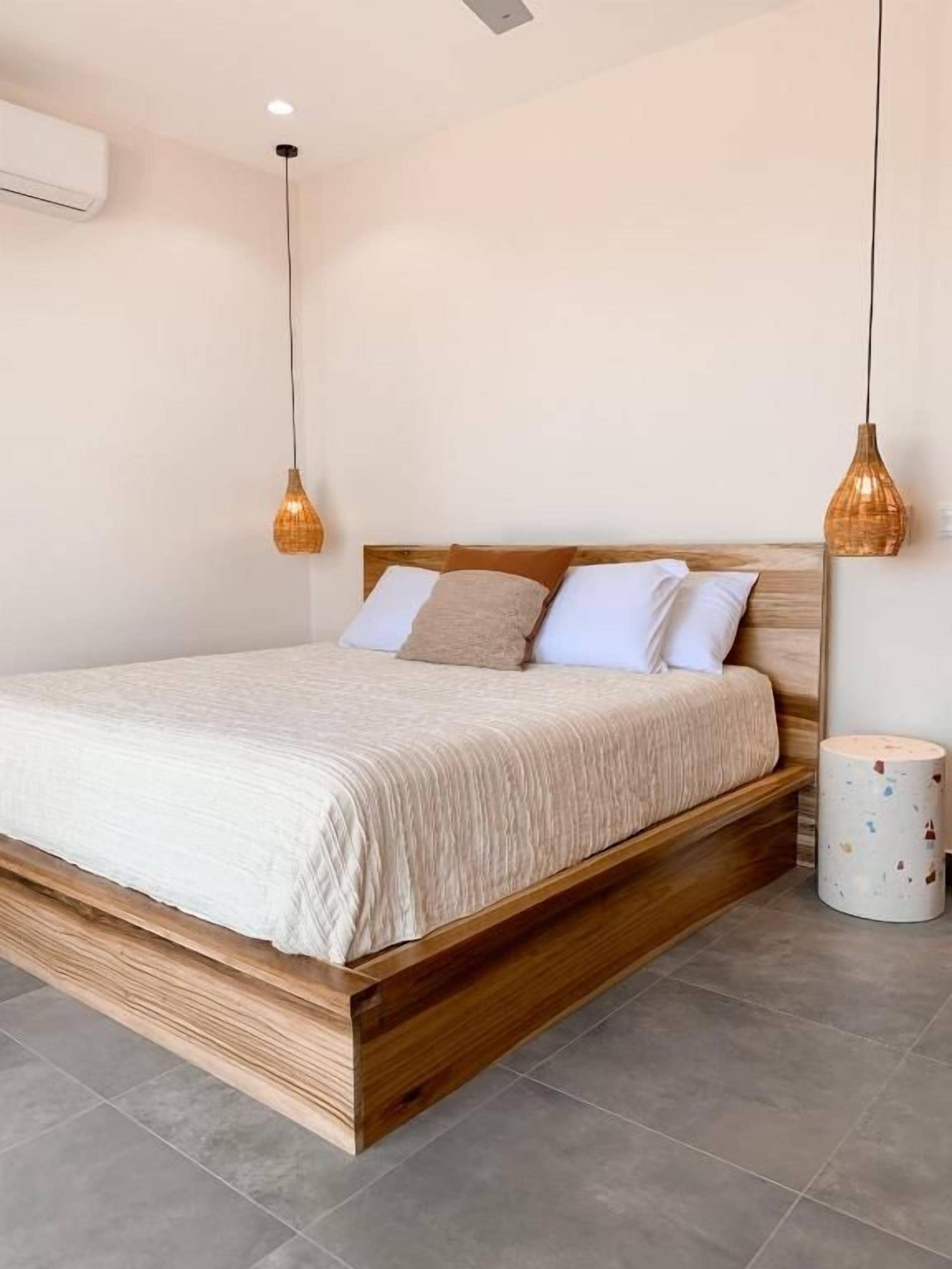 A bedroom with a wooden bed frame, white bedding, and two hanging pendant lights.