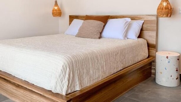 Een slaapkamer met een houten bedframe, witte beddengoed en twee hangende hanglampen.