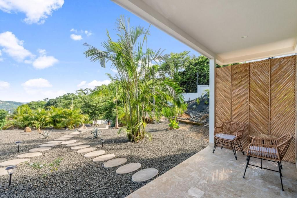 An outdoor patio with a stone pathway, wicker chairs, and tropical plants.