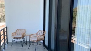 Een balkon met twee rieten stoelen en een tafel, een schuifdeur en een betegelde vloer.