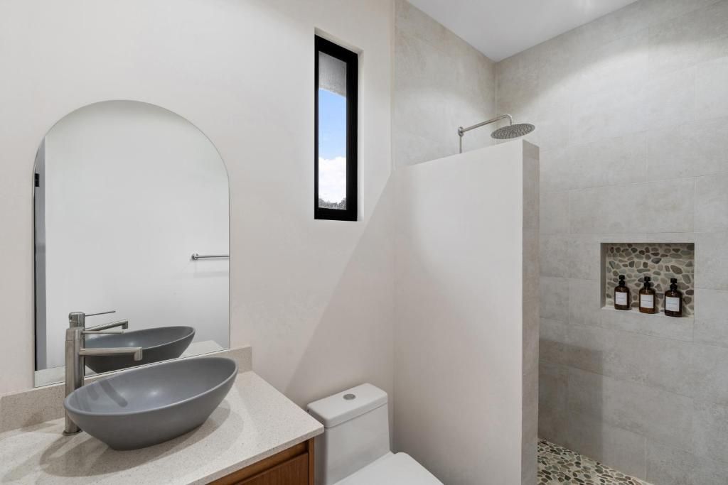 A modern bathroom with a large mirror, a vessel sink, a toilet, and a shower area with stone tiles.