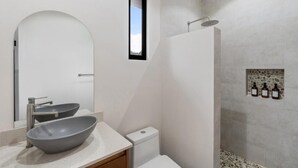Un baño moderno con un espejo grande, un lavabo sobre encimera, un inodoro y una zona de ducha con baldosas de piedra.