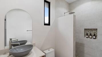 A modern bathroom with a large mirror, a vessel sink, a toilet, and a shower area with stone tiles.