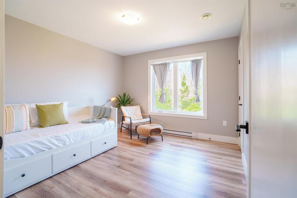 A bedroom with a bed, a chair, a window, and a plant.