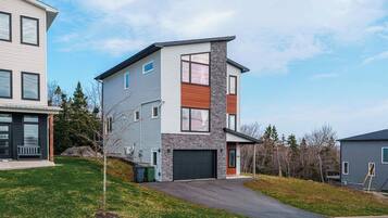 A modern two-story residential building with a garage, a small front yard, and a neighboring house.