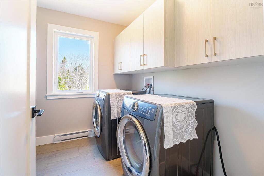 A laundry room with two front-loading washing machines, a window with a view of trees, and light-colored cabinets.