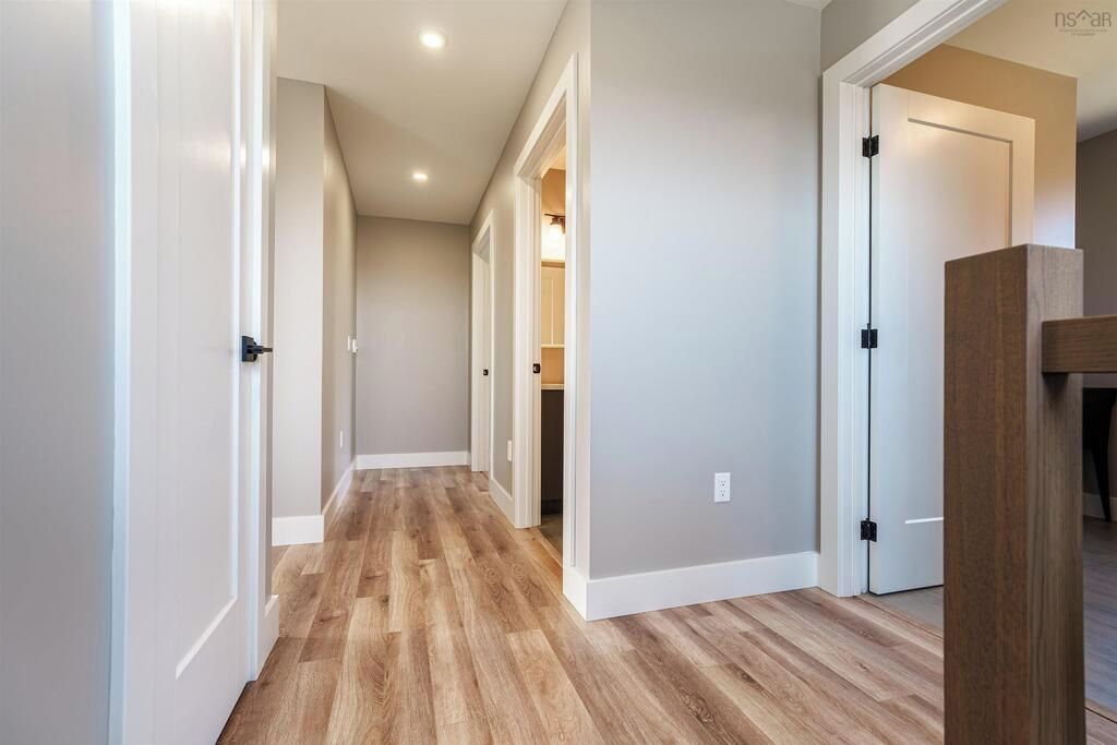 A hallway with wooden flooring, white walls, and doors leading to other rooms.