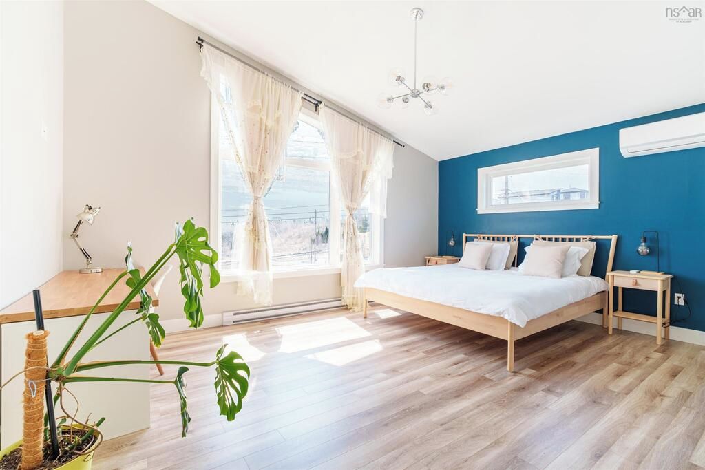 Une chambre à coucher avec un lit, des tables de chevet, une fenêtre avec des rideaux, une plante en pot et une vue sur l’extérieur.