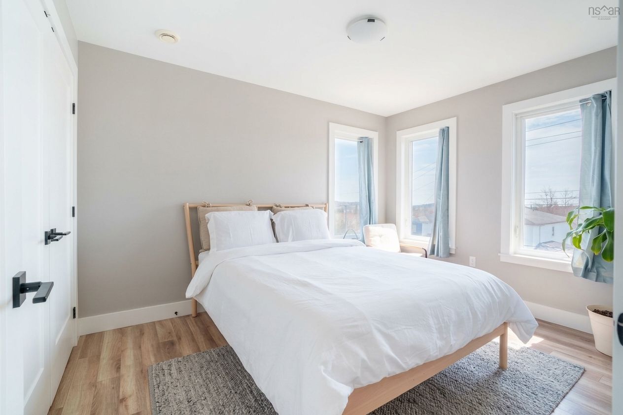 A bedroom with a bed, a nightstand, a window with curtains, a plant, and a door.