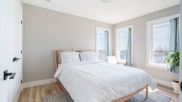 A bedroom with a bed, a nightstand, a window with curtains, a plant, and a door.