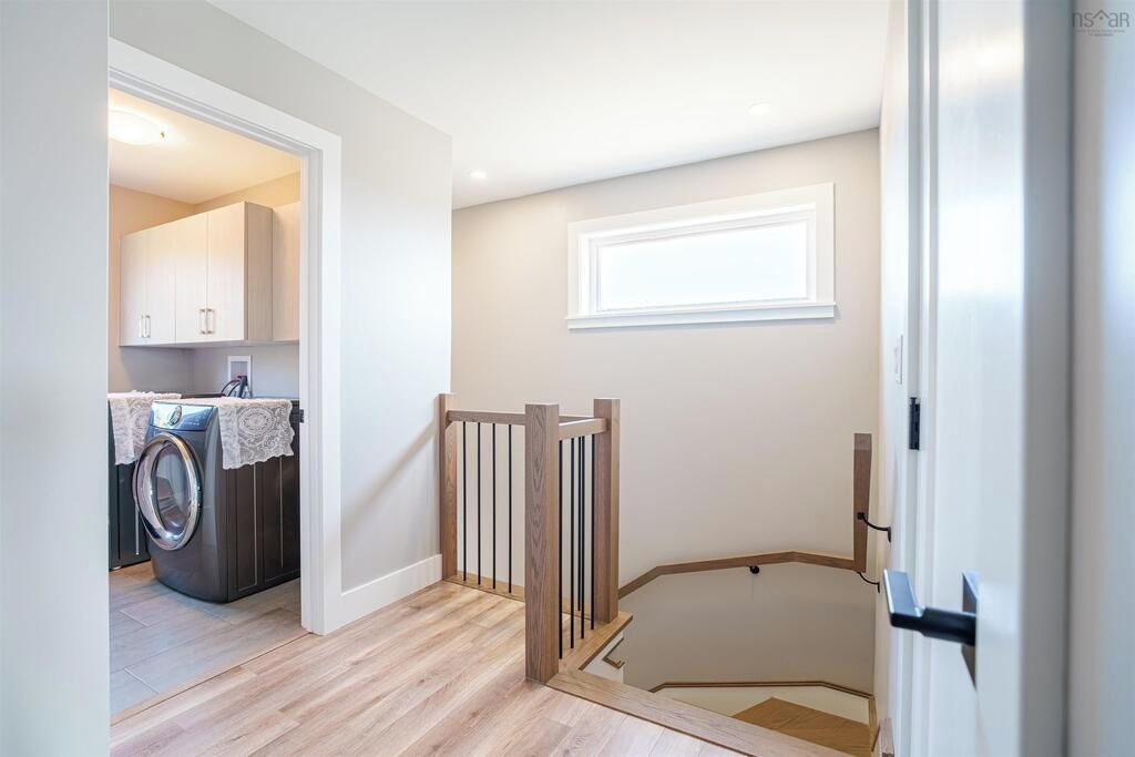 A laundry area with a washing machine, a wooden staircase, and a white wall with a window.