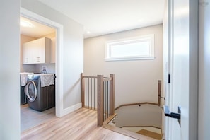 Un área de lavandería con lavadora, una escalera de madera y una pared blanca con ventanal.
