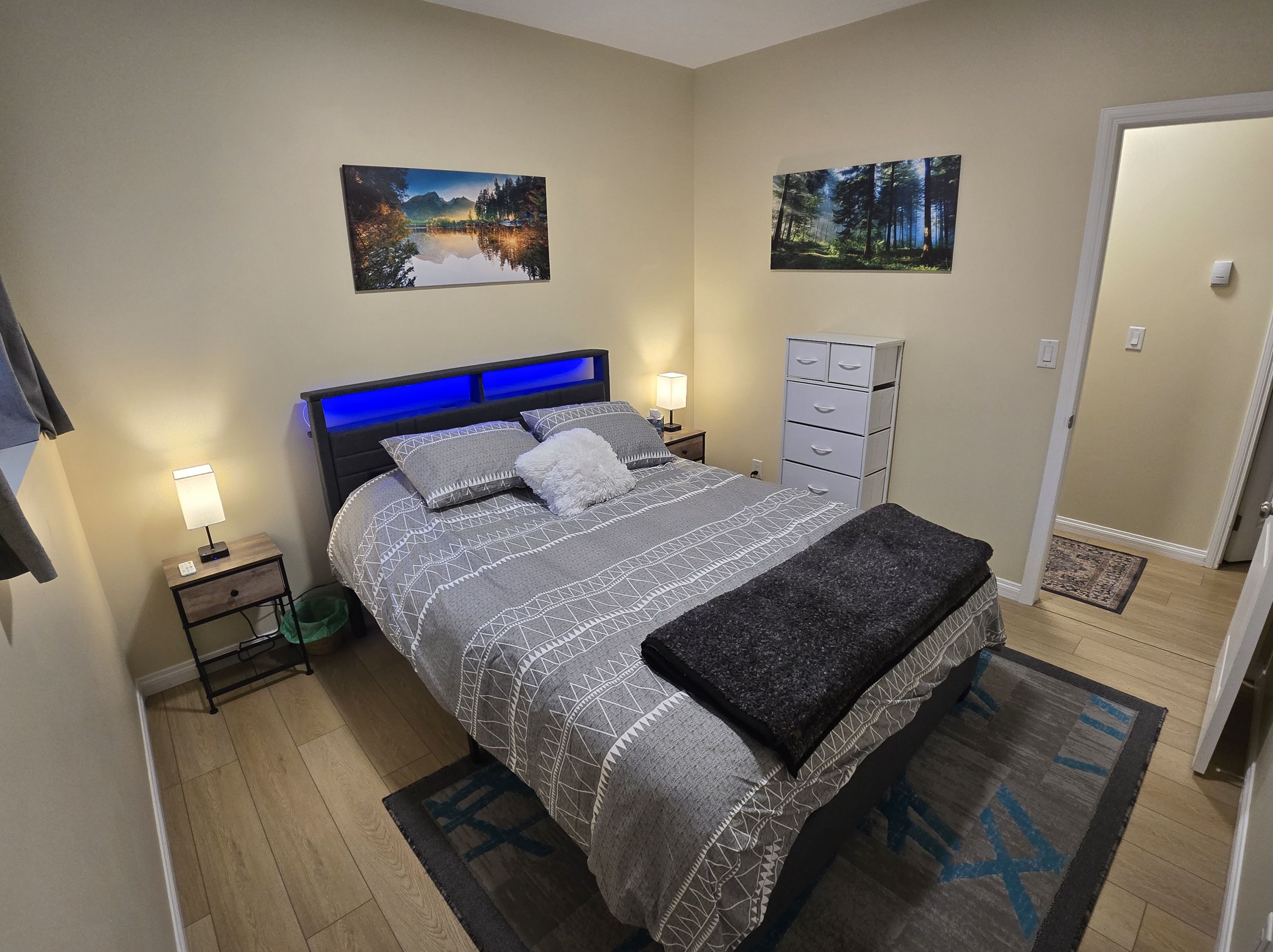 Une chambre à coucher bien rangée, avec un lit, des tables de chevet, une commode, une coiffeuse et deux tableaux accrochés au mur.