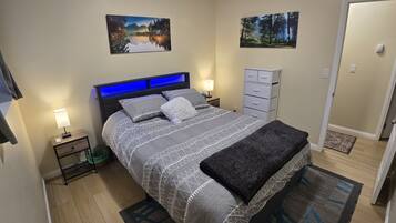 Une chambre à coucher bien rangée, avec un lit, des tables de chevet, une commode, une coiffeuse et deux tableaux accrochés au mur.