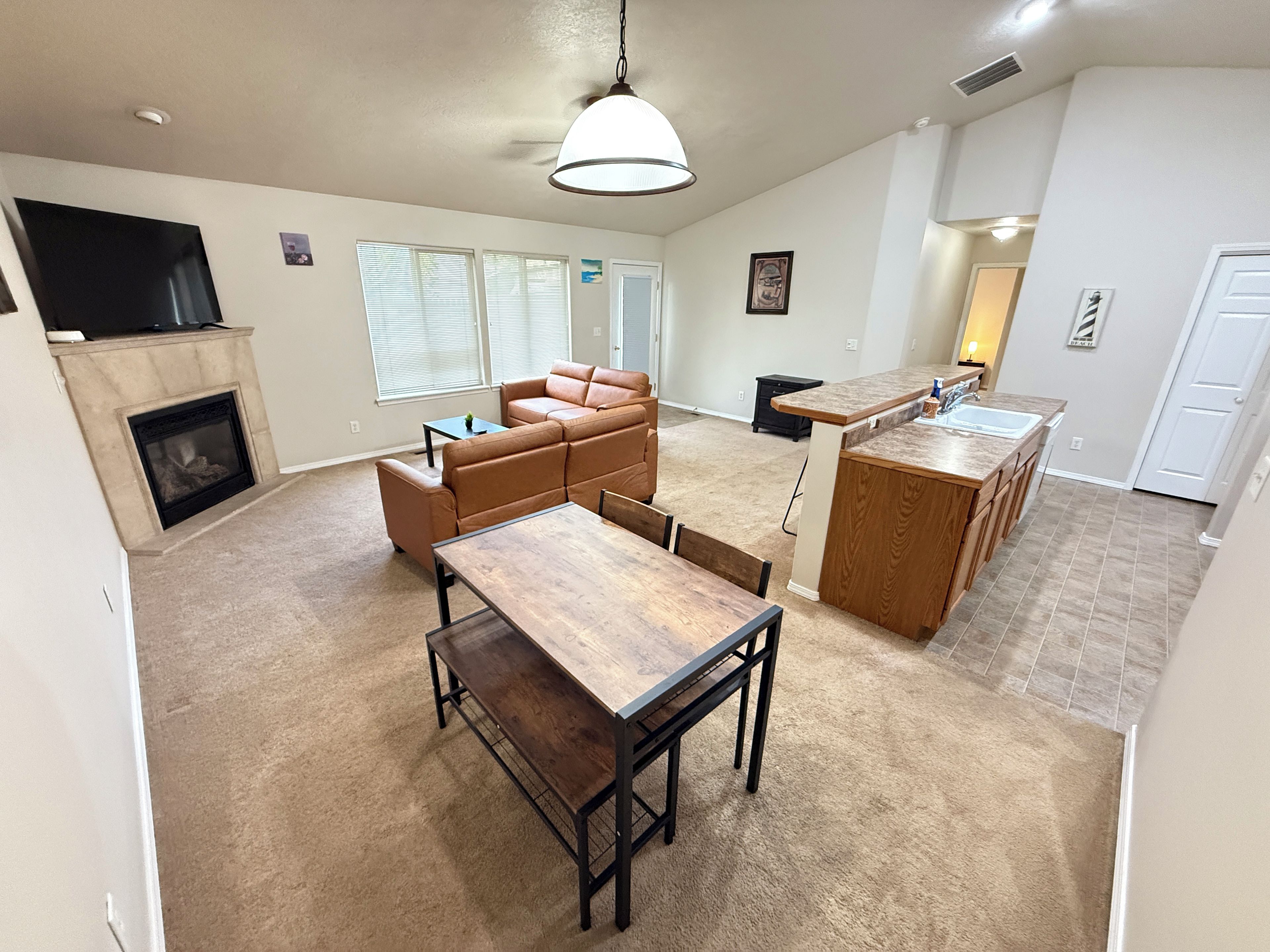 A spacious living room with a fireplace, a dining area, and a kitchen with a bar.