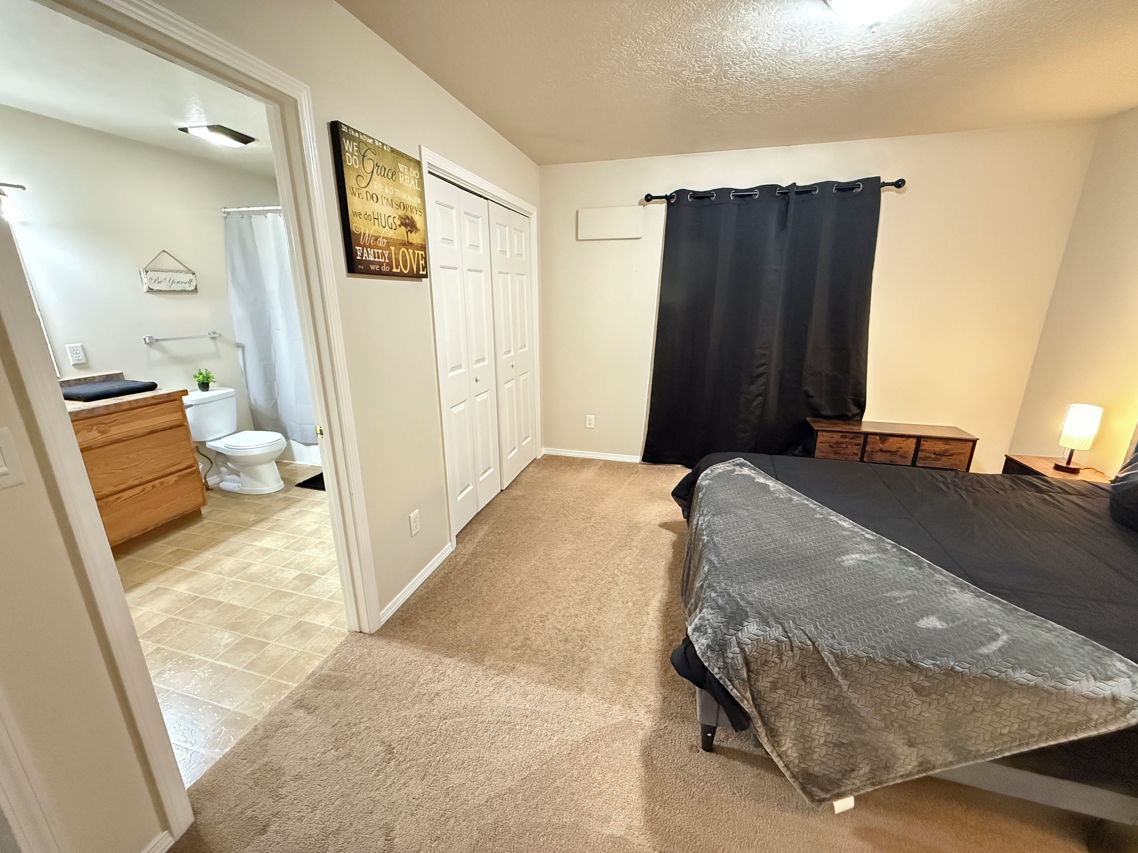 A bedroom with a bed, a nightstand, a dresser, a bathroom with a toilet, and a shower curtain.
