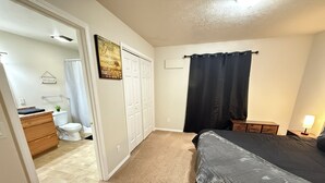 Une chambre à coucher comprenant un lit, une table de chevet, une commode, une salle de bain avec des toilettes et un rideau de douche.