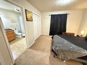 Quarto com cama, mesa de cabeceira, cômoda e banheiro com vaso sanitário e cortina de chuveiro.