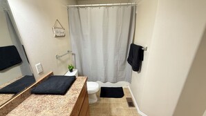 Une salle de bain avec un comptoir en granit, des toilettes, un rideau de douche et un porte-serviettes.