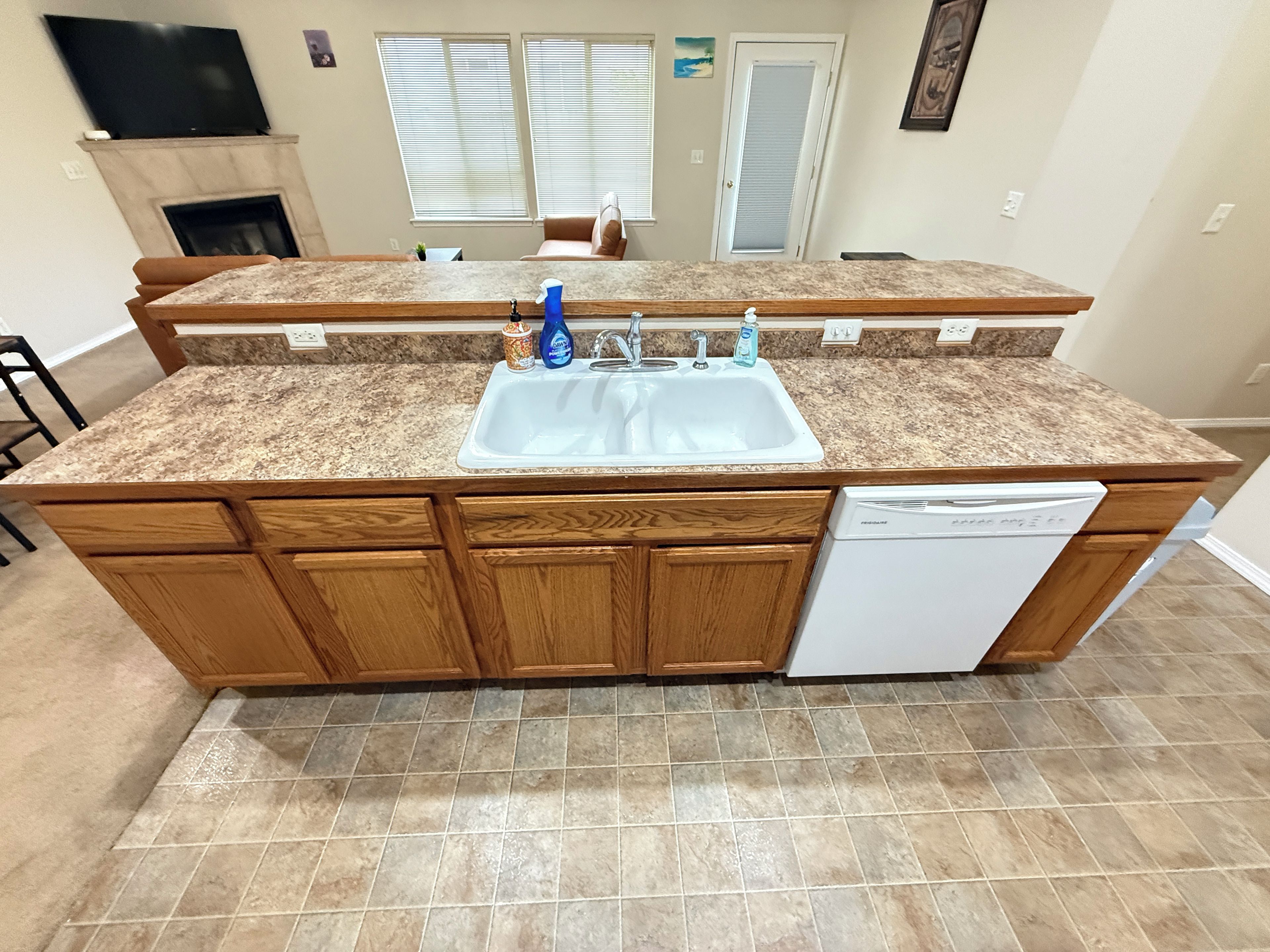Una cocina con encimera de granito, gabinetes de madera, lavavajillas integrado y un lavamanos doble.