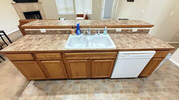 Una cocina con encimera de granito, gabinetes de madera, lavavajillas integrado y un lavamanos doble.