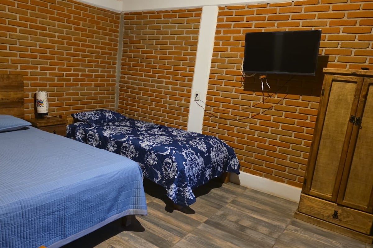 Una habitación con dos camas, un televisor montado en la pared y un armario de madera.