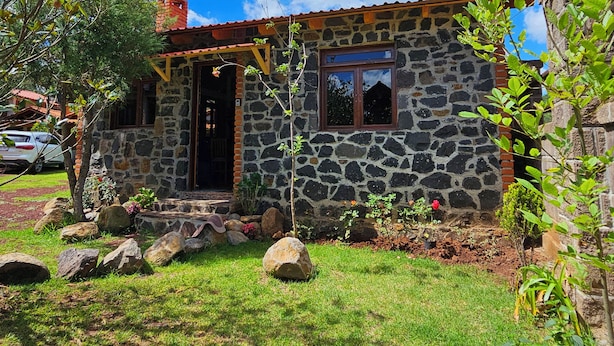 A stone house with a red roof, a wooden door, and a small garden with rocks and plants. - Cabañas JH (Huasca)
