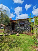 Una casa de piedra con techo rojo, puerta de madera y un pequeño jardín con rocas y plantas.