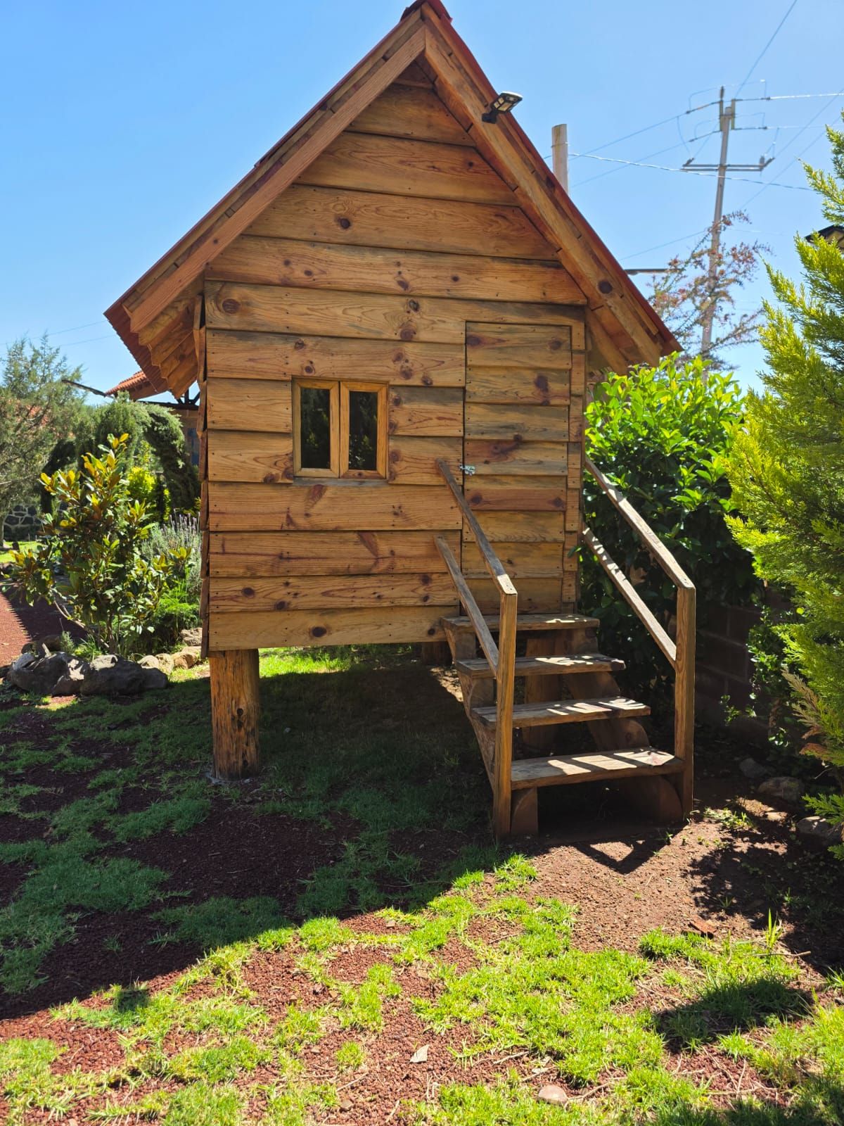 Una cabaña de madera con un ventanal pequeño y una escalera de madera que lleva a la entrada.