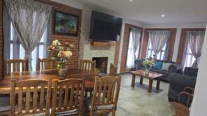 Una sala de estar con chimenea, televisor montado en la pared y comedor con mesa y sillas de madera.