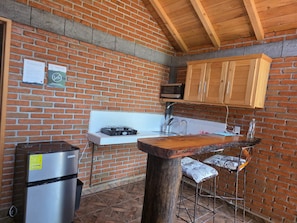 A kitchen with brick walls, wooden cabinets, a stainless steel refrigerator, and a wooden bar stool. - Cabañas JH (Huasca)