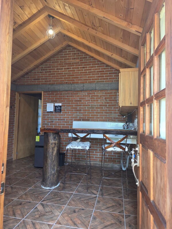 Una cocina rústica con pared de ladrillo, vigas de madera en el techo y una zona de bar con taburetes.