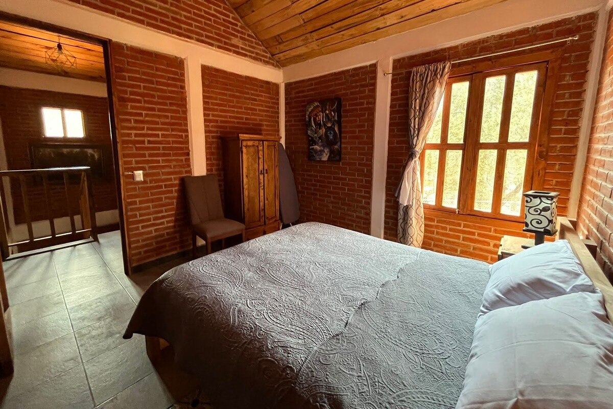 Un dormitorio con cama, una silla, un armario y un ventanal con cortinas.