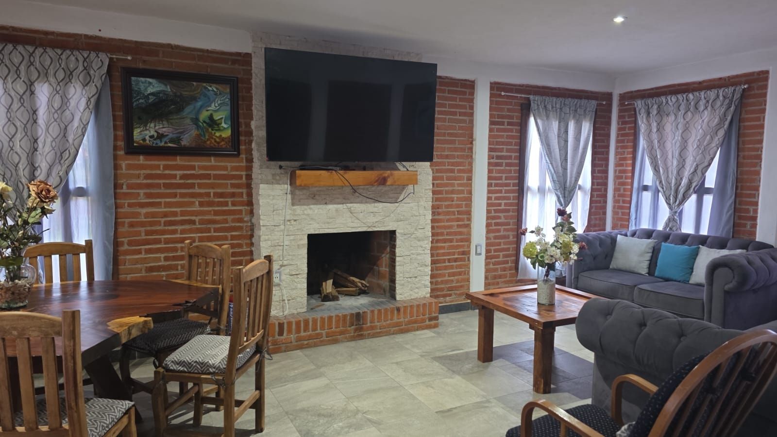 Una sala de estar con chimenea de ladrillo, televisor de pantalla plana montado encima, mesa de comedor con sillas y sofá.