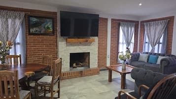 Una sala de estar con chimenea de ladrillo, televisor de pantalla plana montado encima, mesa de comedor con sillas y sofá.