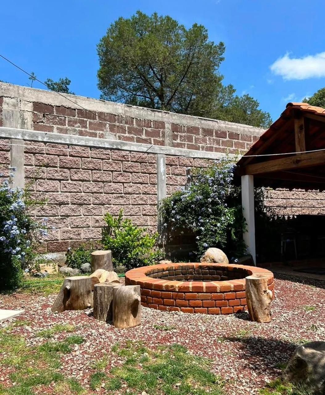 Un hogar de ladrillo rodeado de troncos de madera, frente a un muro de ladrillo bajo un cielo despejado.